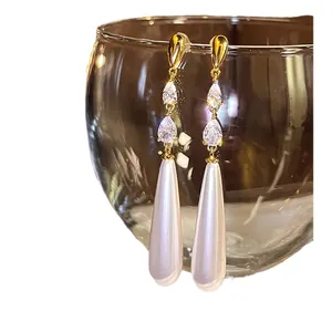 Élégantes boucles d'oreilles dorées avec zircons étincelants et longues perles blanches.