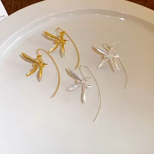 Eleganti orecchini a gancio con fiori di iris in oro e argento su un piatto beige minimalista