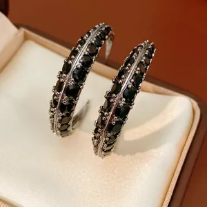 Close-up detail of silver hoop earrings featuring double rows of black zircon stones.
