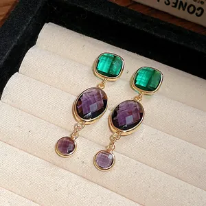 Close-up of vintage gold-tone earrings with green and purple zircon stones in a tray