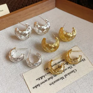 Primer plano de pendientes de botón en forma de C con textura tejida en plata y oro.