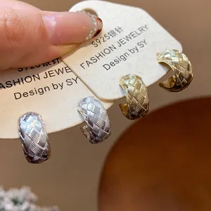 Primer plano de pendientes en forma de C con textura de tejido cruzado en oro y plata.