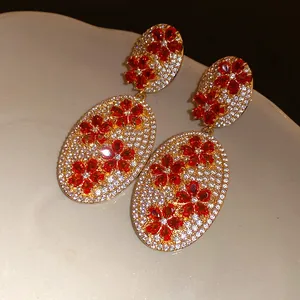 Close-up of vintage gold earrings with white pavé zircons and red floral patterns