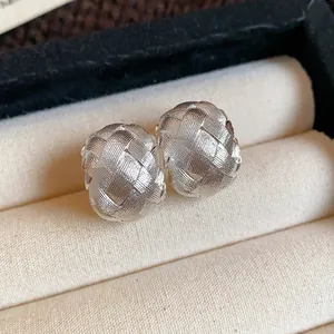Vista detallada de pendientes en C plateados con textura tejida dentro de un joyero
