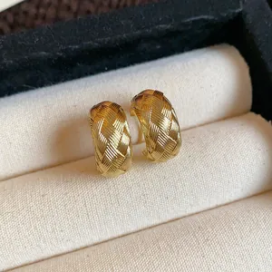 Primer plano de pendientes de botón en forma de C dorados con textura tejida cruzada