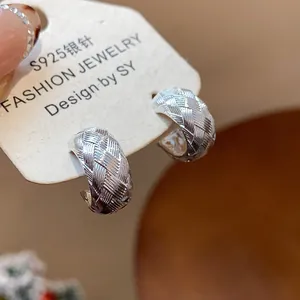 Primer plano de pendientes en C minimalistas con textura cruzada y aguja de plata S925