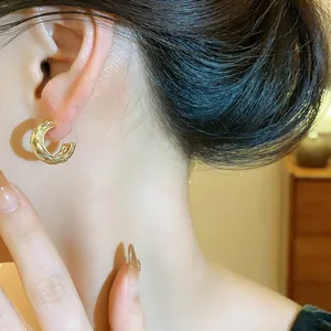 Detalle de elegantes pendientes de aro dorados en forma de C con textura cruzada en la oreja.
