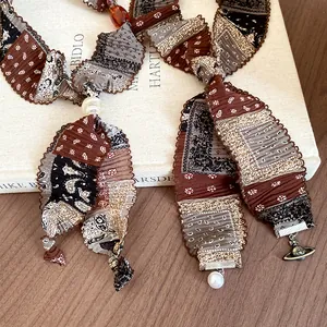 Close-up detail of ethnic pleated fabric necklace with pearl and Saturn orb metal pendant