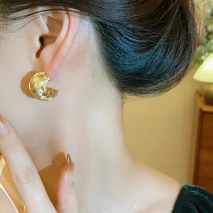 Elegantes pendientes de botón dorados en forma de C con textura cruzada en una modelo