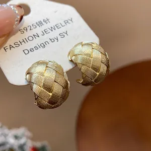 Primer plano de pendientes en C dorados con textura tejida y aguja de plata S925.