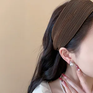 Close-up of elegant brown pleated wide headband worn by model with pearl jewelry