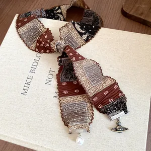 Detailed view of an ethnic fabric ribbon necklace with a Saturn pendant and pearl.