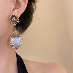 Nahaufnahme von Vintage-Blumen-Ohrhängern mit einer leuchtenden Perlenkugel und Silbernadel.