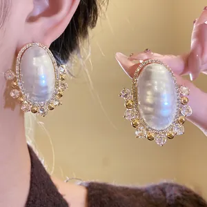Close-up of luxury iridescent pearl earrings with zircon halo and gold accents.