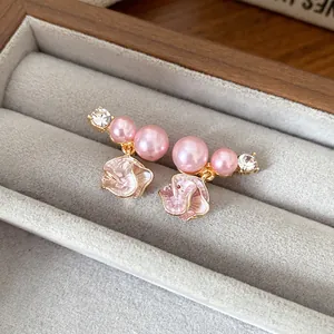 Close-up of elegant pink pearl flower earrings with rhinestone accents in a velvet box.