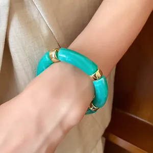 Detail shot of a cyan acrylic marbled tube bracelet with gold metal spacers on a wrist