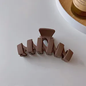 Vue détaillée d'une pince à cheveux mate marron ondulée sur fond blanc minimaliste