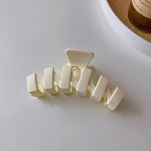 Gros plan d'une pince à cheveux ondulée crème sur un fond blanc minimaliste