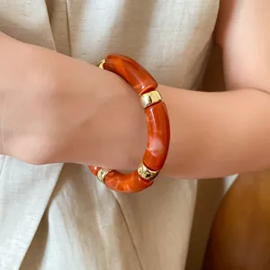 Macro view of an orange marbled acrylic bracelet with gold-tone segments.