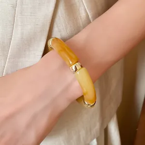 Detailed view of an acrylic iridescent spliced bracelet in amber yellow and gold