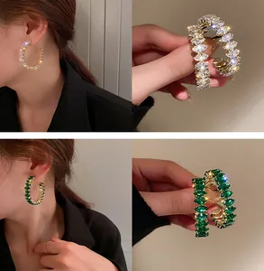 Dettaglio elegante di orecchini a cerchio dorati con pietre bianche e verde smeraldo