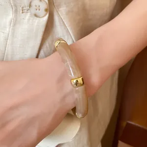 Close-up detail of a marbled beige acrylic bracelet with elegant gold segments on wrist