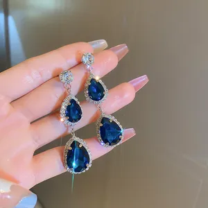 Elegant silver needle drop earrings featuring blue teardrop zircon stones with pavé halo