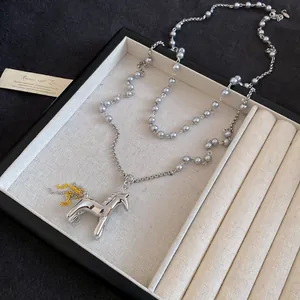 Détail d'un collier pendentif cheval en argent poli avec des perles grises dans un plateau