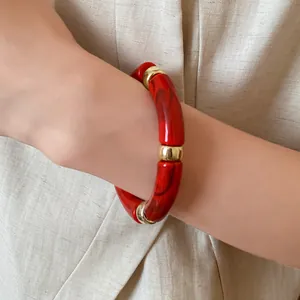 Close-up of a red marbled acrylic bangle bracelet worn on a wrist over linen clothing.
