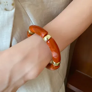 Detail view of a marbled orange acrylic bracelet with gold-tone spacers on a wrist.