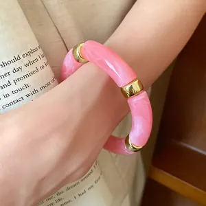 Detailed macro view of a pink marbled acrylic and gold-toned segment bracelet worn on wrist