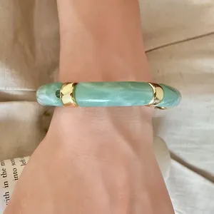 Macro view of vintage green marbled acrylic bamboo bracelet with gold accents on a wrist