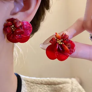 Primo piano di orecchini a fiore in conchiglia rossa vintage con occhio di tigre e grani d'oro.