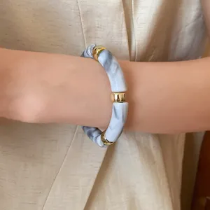 Close-up view of a marble-textured acrylic tube bracelet with gold metal accents on wrist.