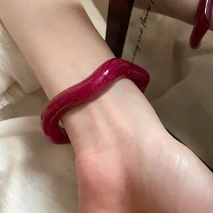 Gros plan d'un bracelet jonc ondulé en résine bordeaux brillant porté au poignet