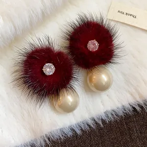 Dettaglio macro di orecchini di peluche con pelliccia rossa e perla crema.