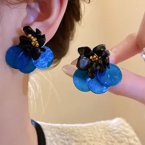 Dettaglio di orecchini a fiore vintage con conchiglie blu e pietre occhio di tigre.