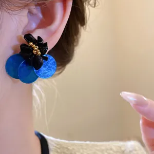 Dettaglio di orecchini a fiore vintage con dischi in conchiglia blu e perni d'argento.