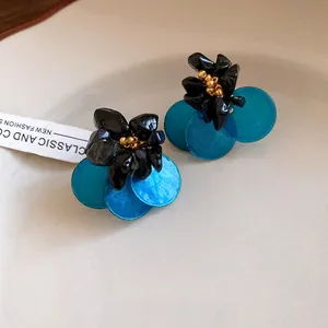 Primo piano di orecchini a fiore con dischi di conchiglia blu e petali neri opachi