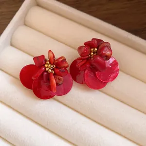 Primo piano di orecchini vintage a fiore in conchiglia rossa con perline dorate.