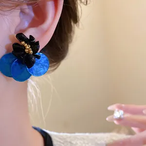 Dettaglio di orecchini a fiore nero con dischi di conchiglia blu su un orecchio reale