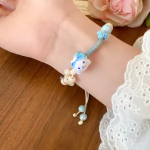Close-up view of a cute ceramic cartoon cat charm on a blue braided wax cord bracelet