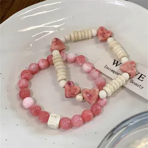 Detailed macro view of pink heart-shaped ceramic and round beaded bracelets on a white plate.