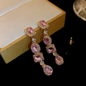Vista dettagliata di eleganti orecchini a pendolo dorati con gemme rosa e accenti di strass