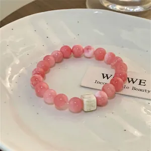 Detail of a pink ceramic bead bracelet with a square marble bead on a white plate