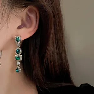 Dettaglio ravvicinato di orecchini geometrici pendenti con cristalli verdi in stile vintage