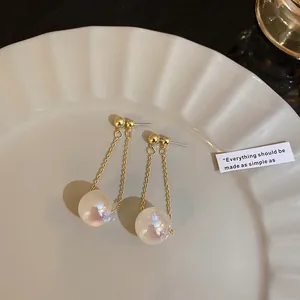 Elegant iridescent mermaid pearl drop earrings with gold chains on a scalloped plate