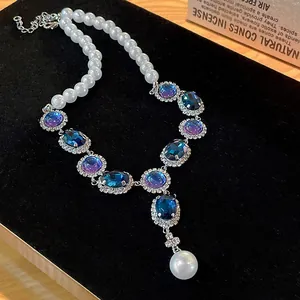 Close-up of vintage pearl necklace with blue crystal oval pendants and rhinestones.