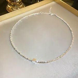 Close-up of minimalist silver necklace with a small cube pendant on a metal tray.