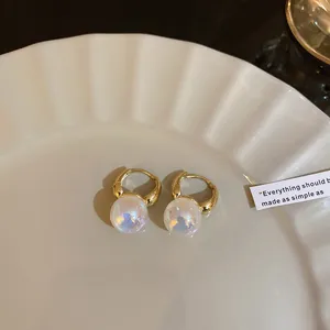 Close-up of aurora pearl hoop earrings with elegant golden finish on white plate.